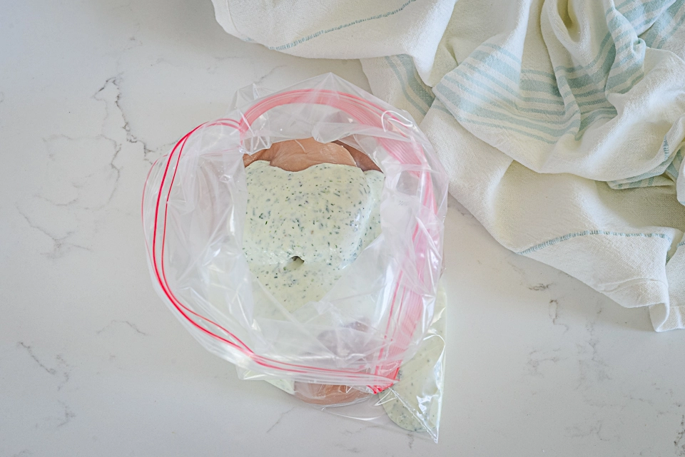 Chicken breasts marinated in sauce, placed in a plastic bag.
