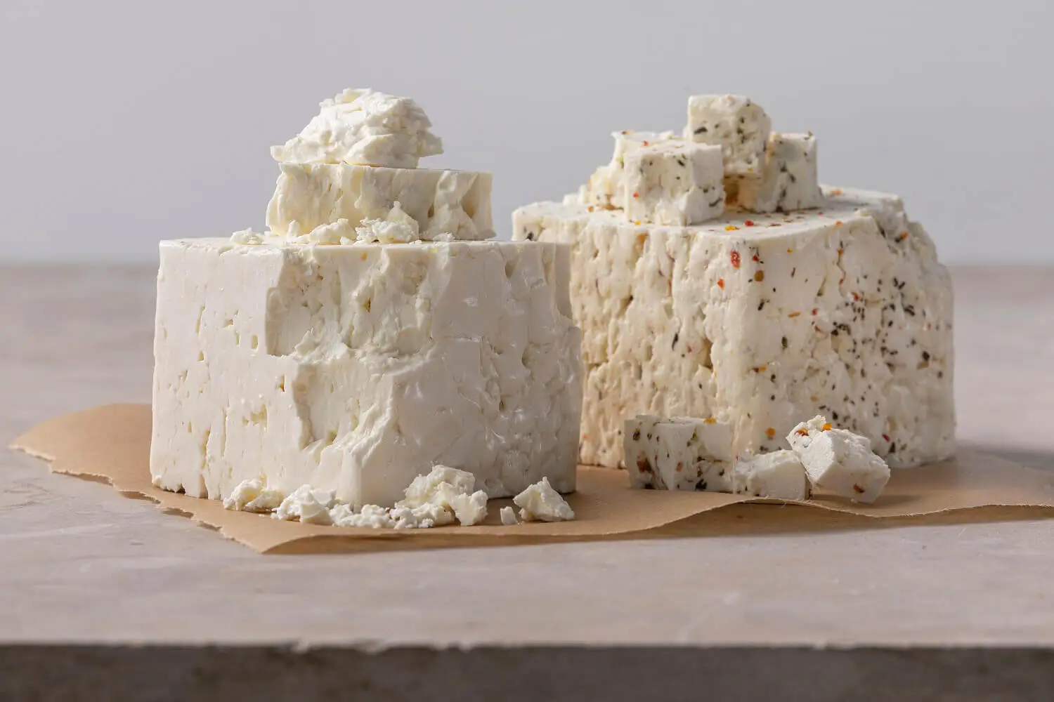 Two blocks of shredded feta cheese on brown paper.