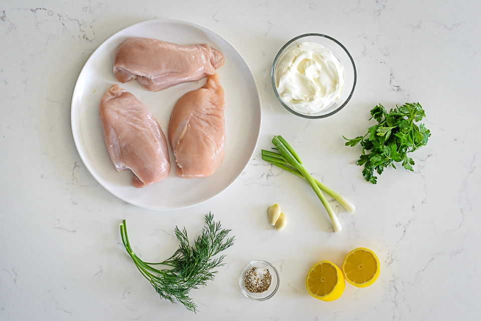 Ingredients for grilled chicken wrap including raw chicken breasts, sour cream, herbs, garlic, and lemon.